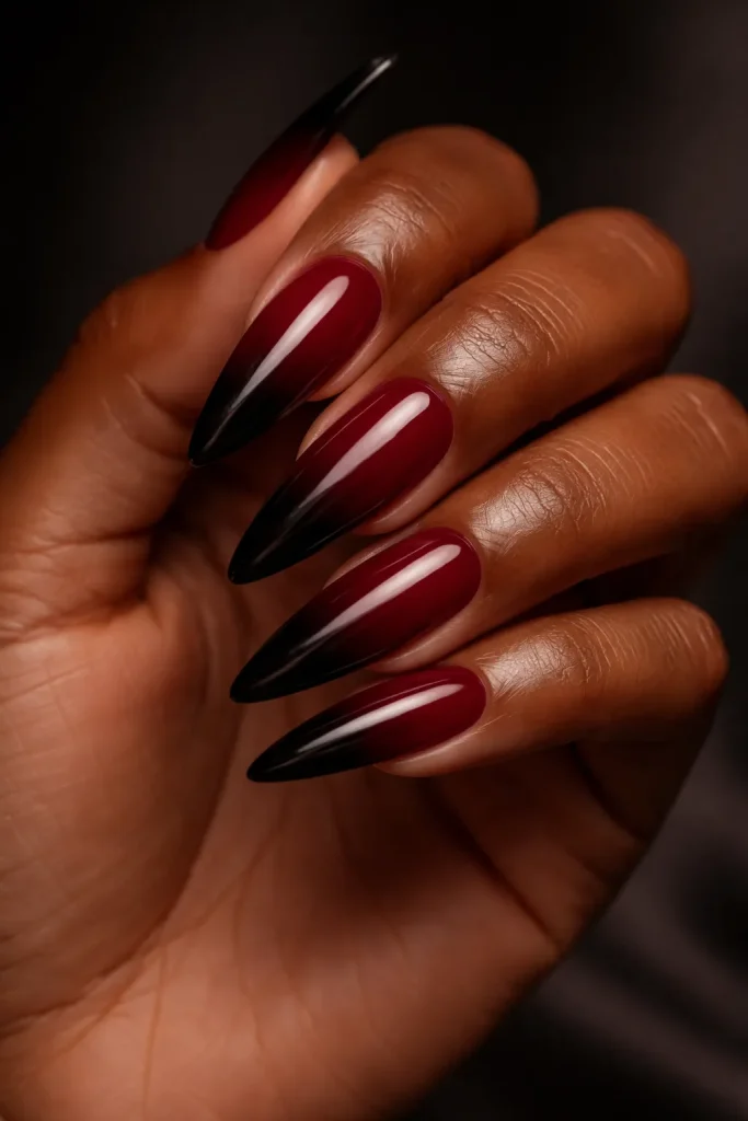 Long stiletto nails featuring a smooth ombre gradient from burgundy to midnight black.