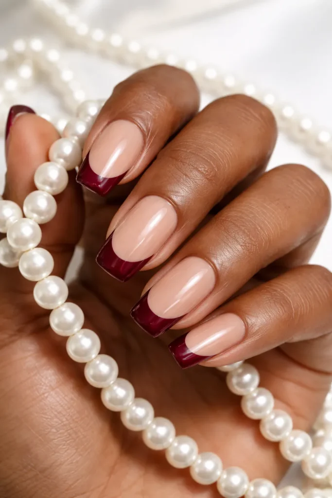 Modern French manicure featuring deep burgundy tips and a nude base on brown skin.