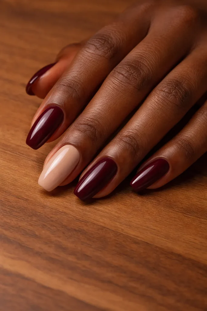 Alternating burgundy and nude colored nails on a hand with rich dark melanin skin.