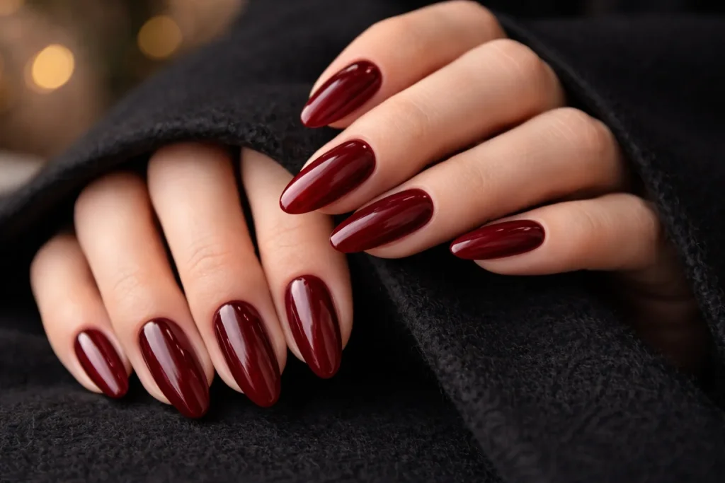 Glossy deep red almond shaped nails resting on a black winter coat.