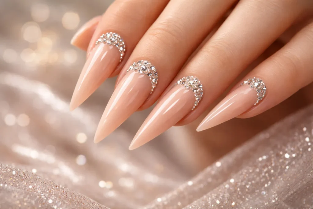 Nude stiletto nails decorated with sparkling clear rhinestones at the base