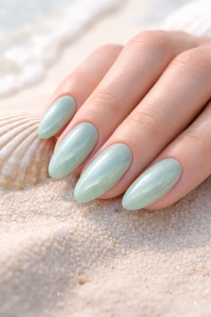 Soft seafoam green cat eye nails with a delicate shimmer on a beach background.