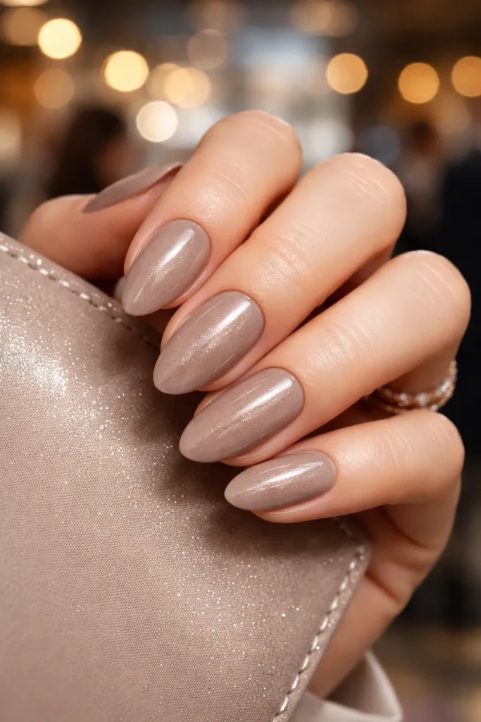 Taupe manicure with subtle champagne shimmer on professional hands in soft lighting