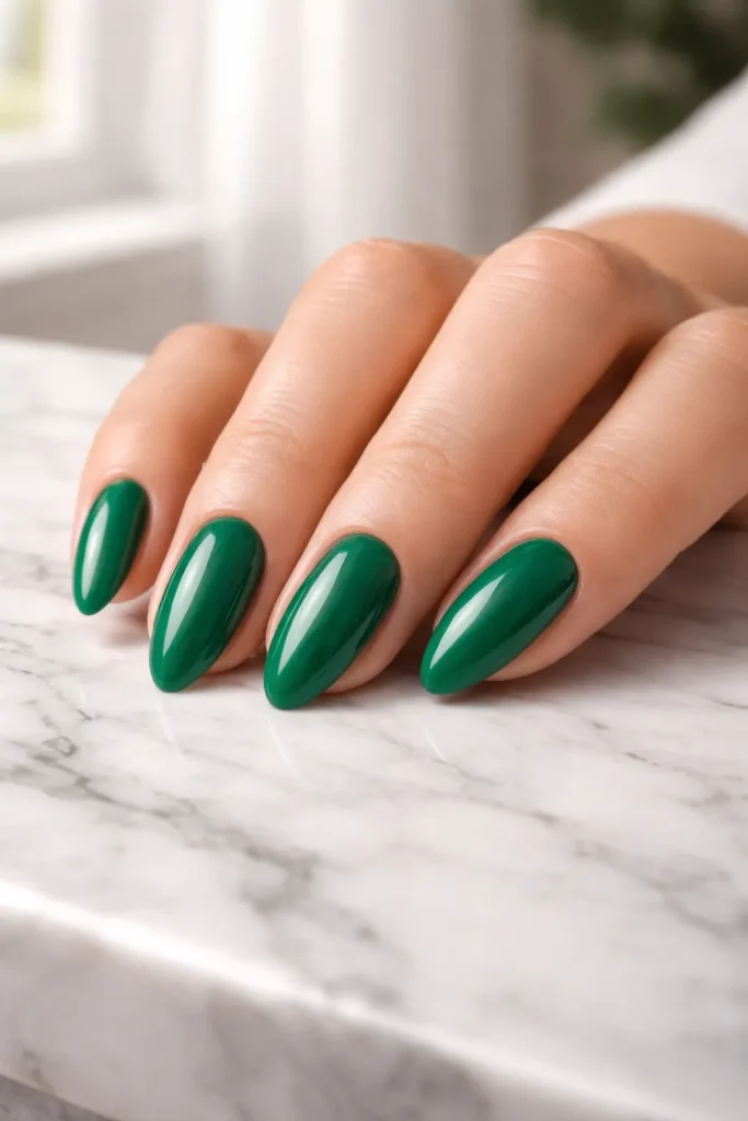 Close up of a hand with solid emerald green glossy nails on a marble surface