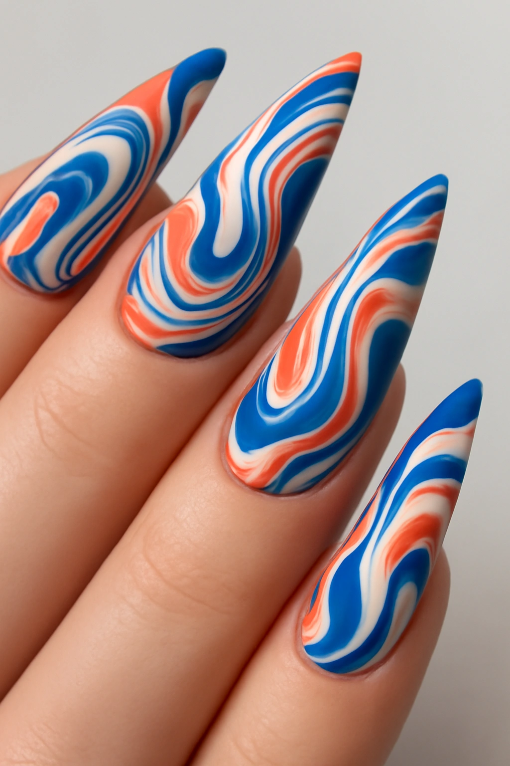 Modern nail art with blue and coral abstract swirls on long stiletto nails.