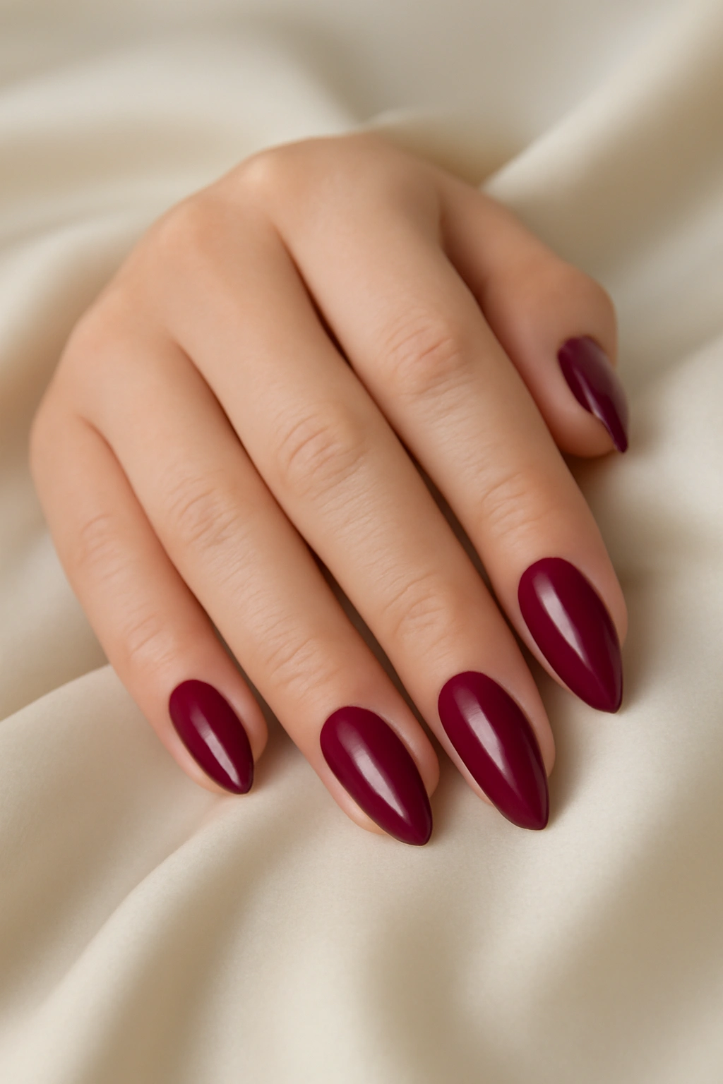 Close up of almond shaped nails painted in solid glossy deep berry polish