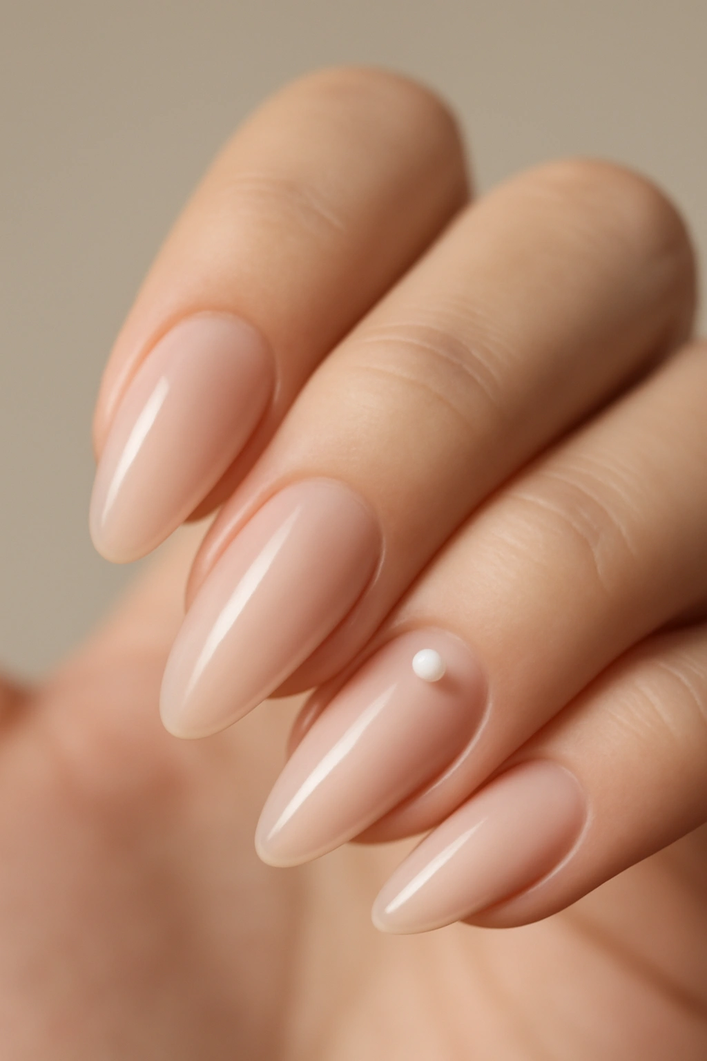 Close-up of almond nails with sheer pink polish and a tiny pearl near the cuticle on one or two nails