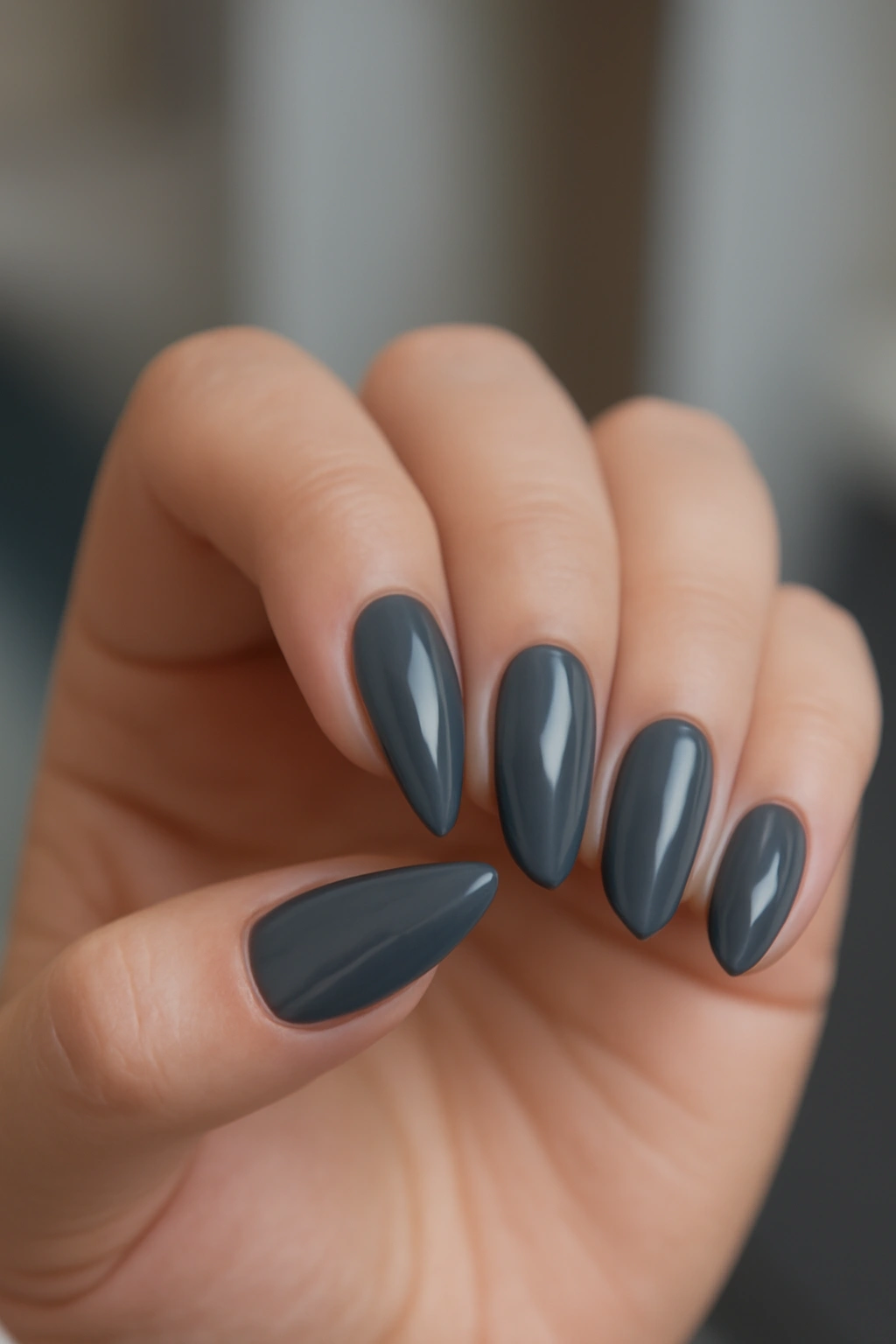 Lipstick shaped nails with slate grey polish on a hand with fuller fingers.