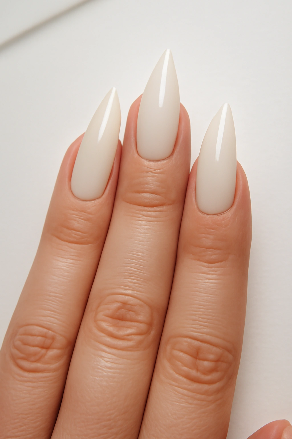 Mountain peak shaped nails with cream polish on a hand with fuller fingers.