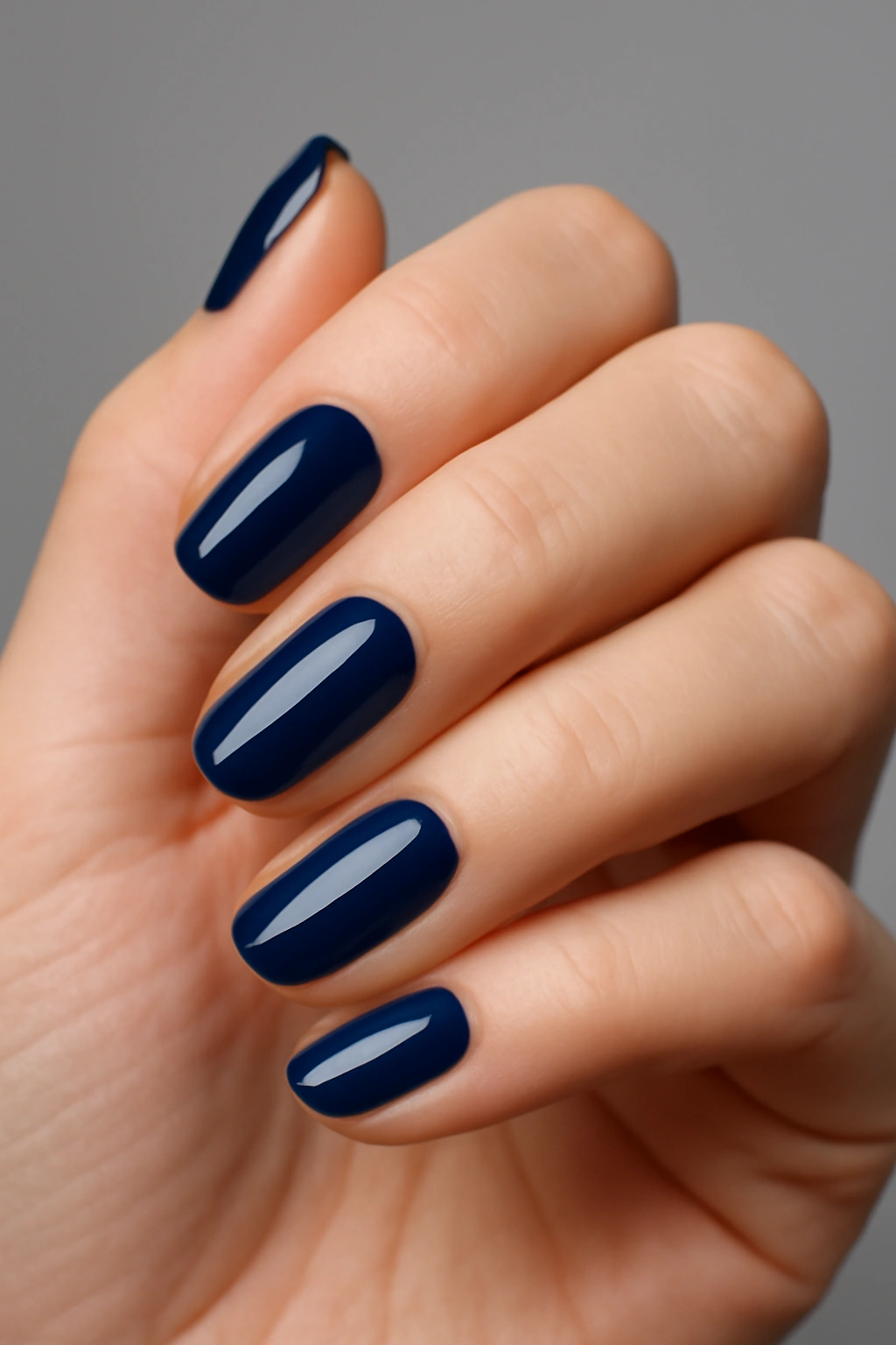 Deep navy blue manicured nails on a woman's hand with a silver ring.