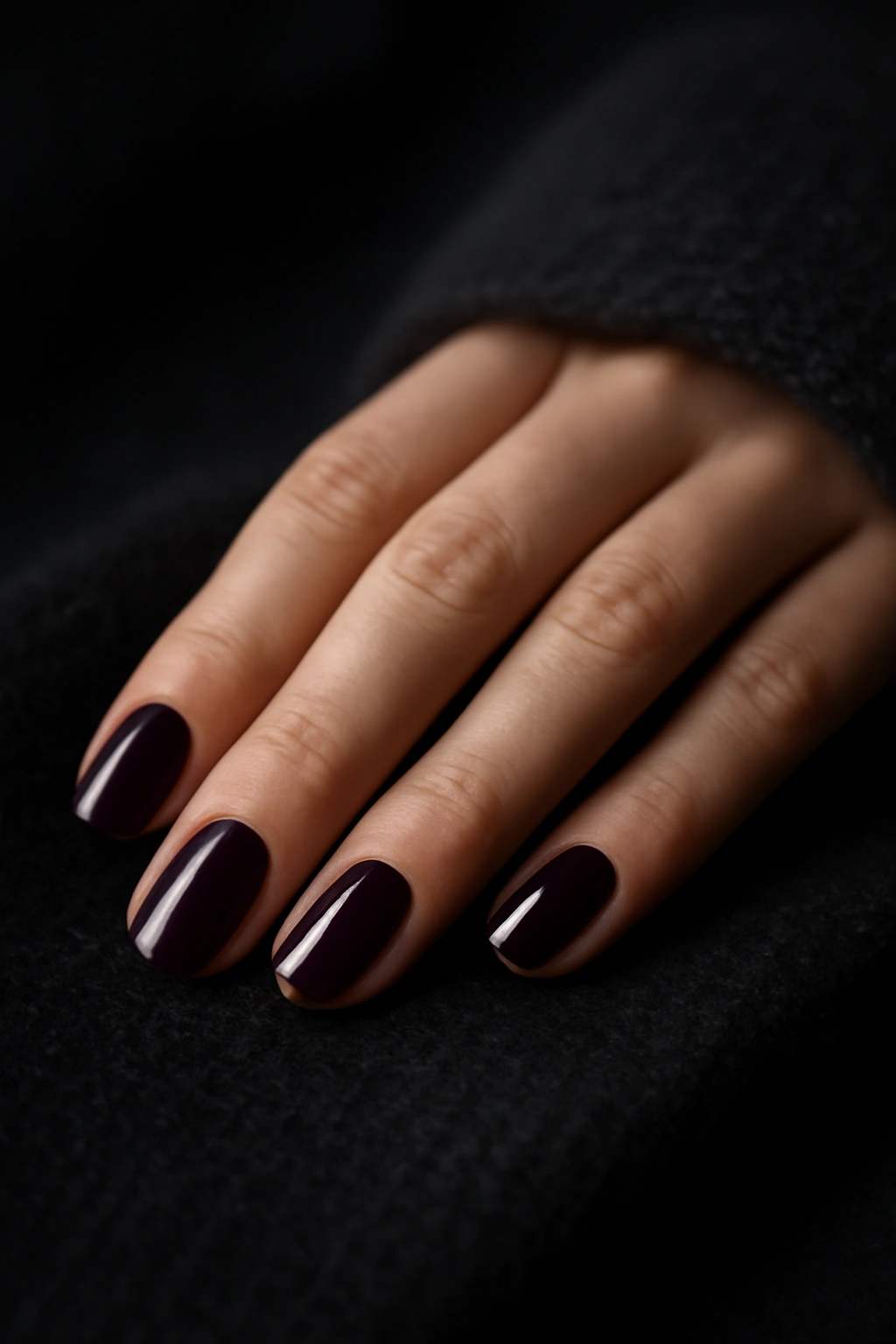 High-gloss deep plum purple nail polish on hands resting on cashmere.