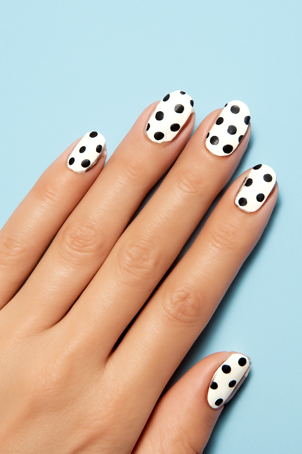 Elegant white nails with black polka dot patterns in a clean minimalist style