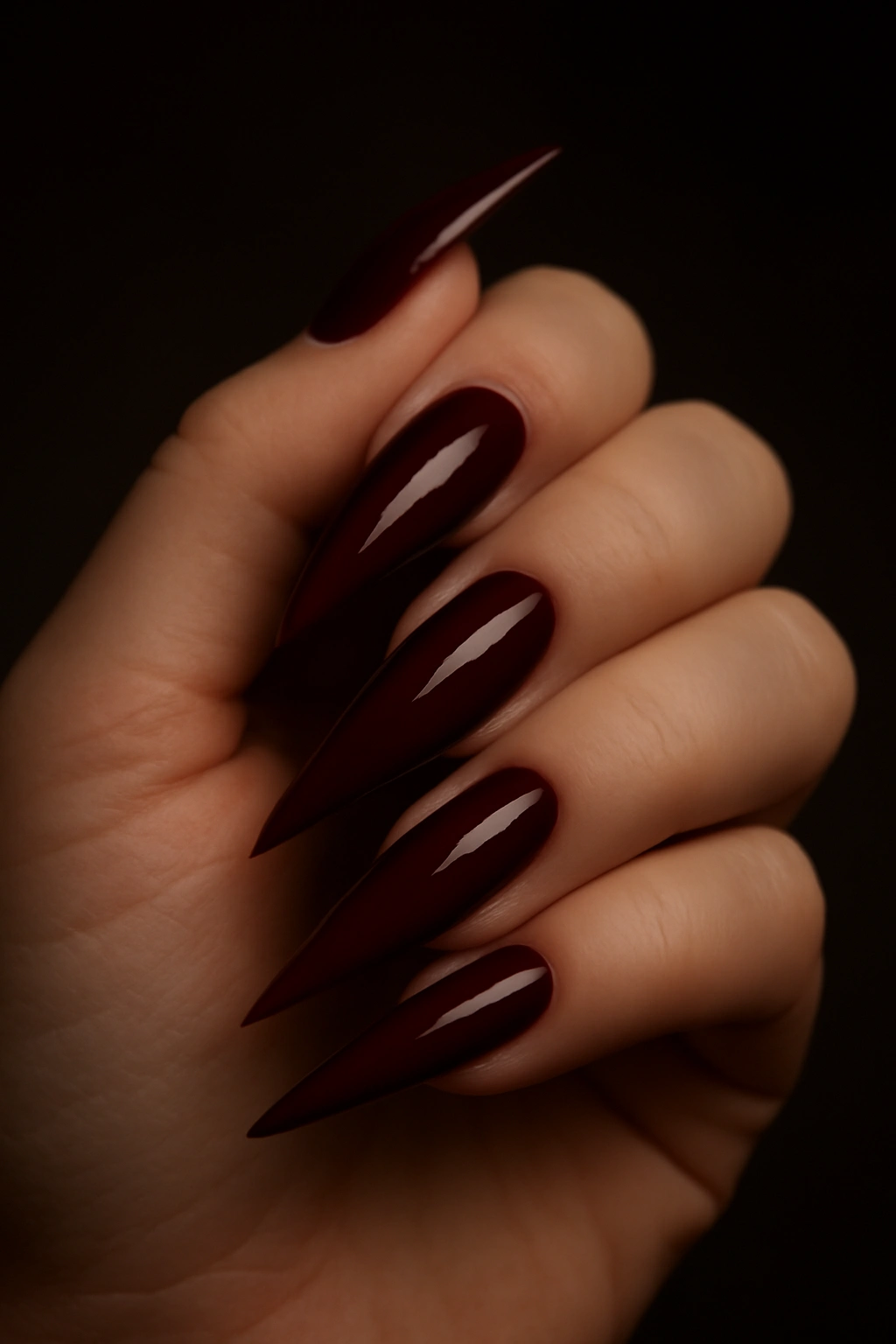 Long stiletto nails in burgundy on a full hand featuring dramatic sharp pointed tips.